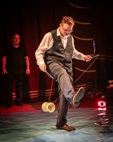 Zirkusartist balanciert eine Diabolo mit einem Fuß auf einer Bühne.